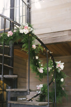 Soft green garland wrapped around the banister for this farm wedding was made even more romantic with the addition of soft greens and pinks