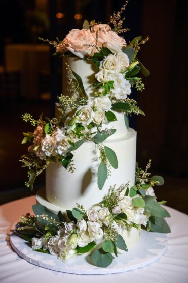 White wedding cake covered in roses and greenery