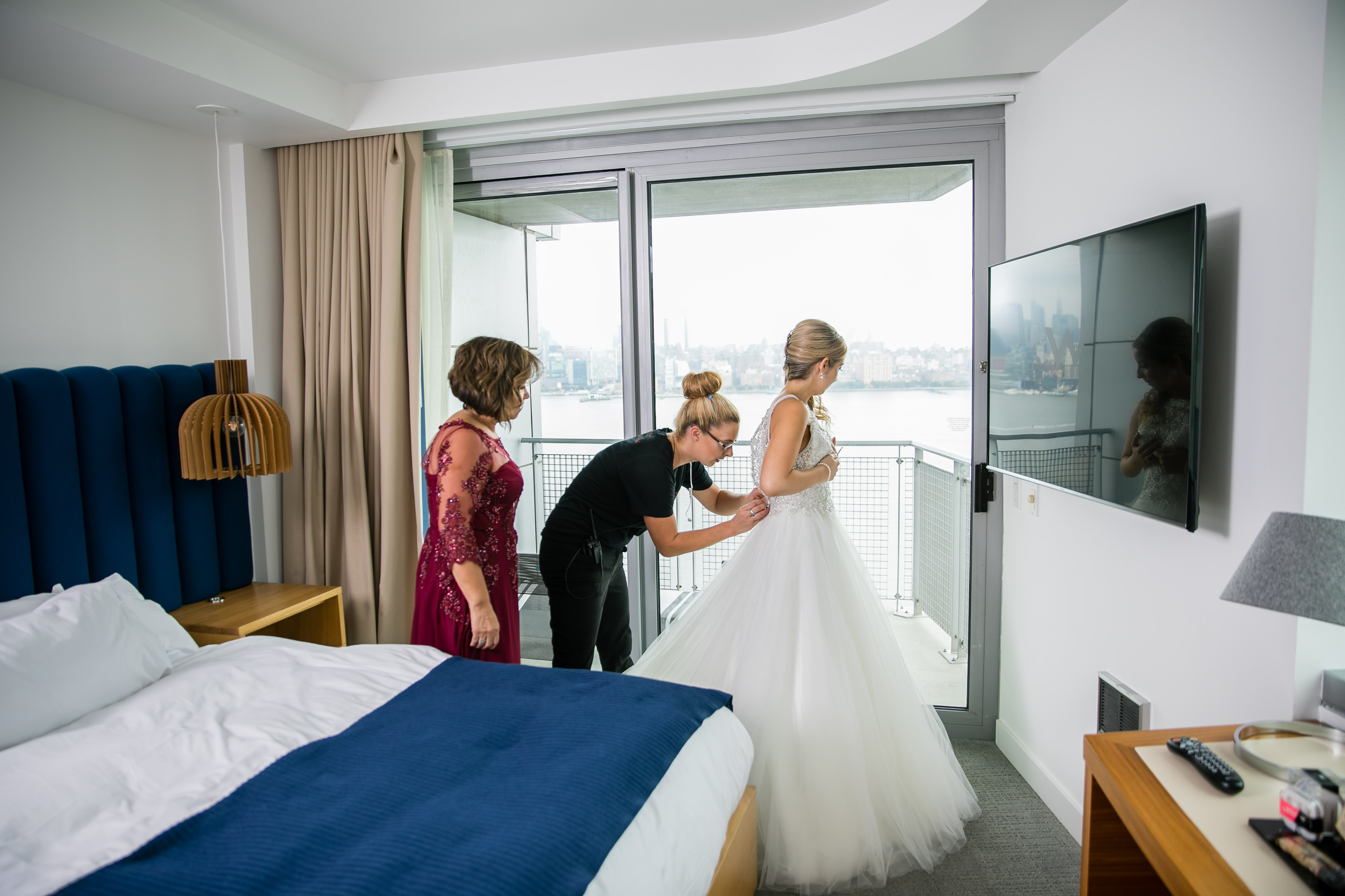 wedding planner zipping up bride's dress with mother of the bride