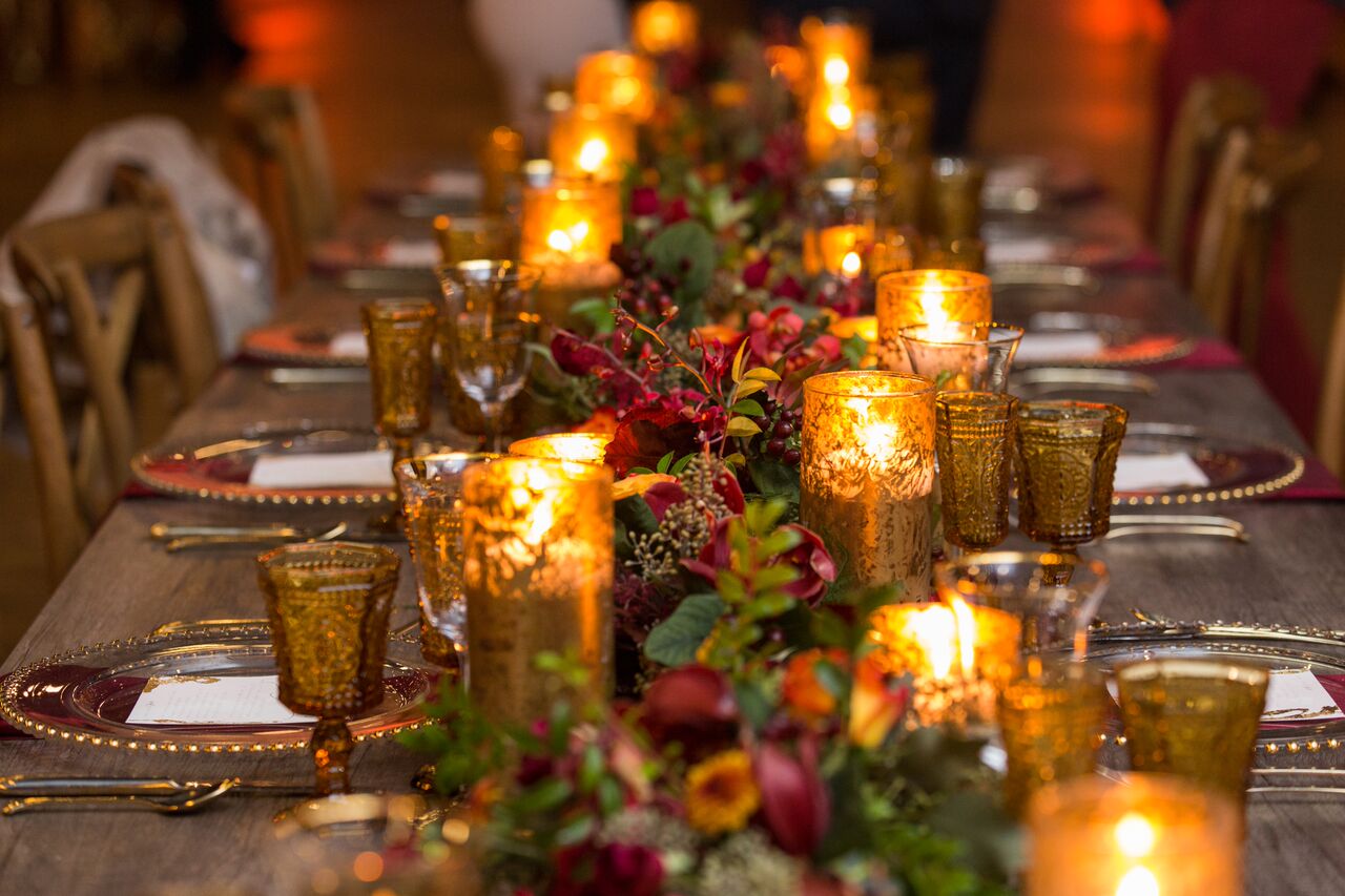 long farmhouse table with green garland and red flowers with gold candles down middle
