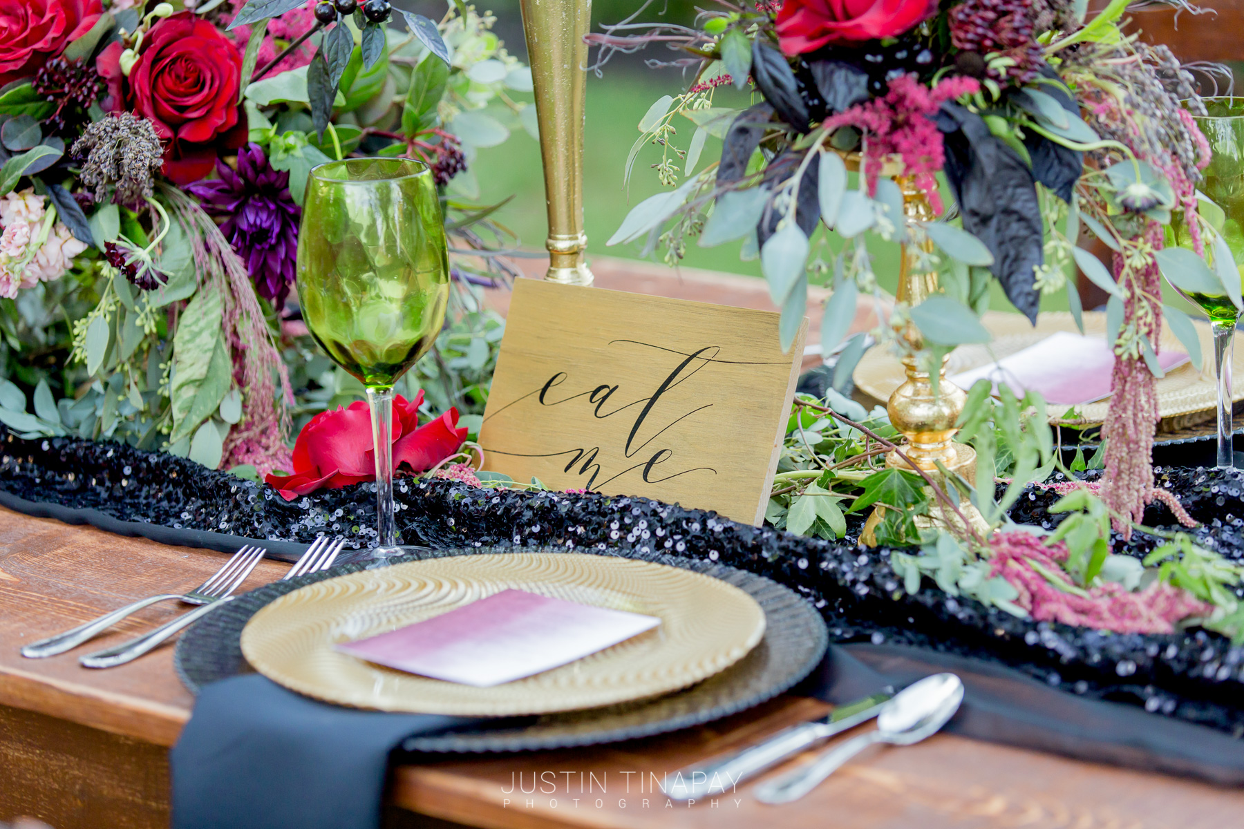 black and gold plates with black sequin runner on farmhouse table and red, purple, and green flowers