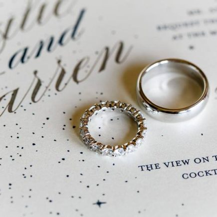 silver and diamond wedding bands on top of sparkly wedding invitation