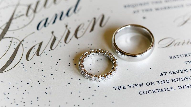 silver and diamond wedding bands on top of sparkly wedding invitation