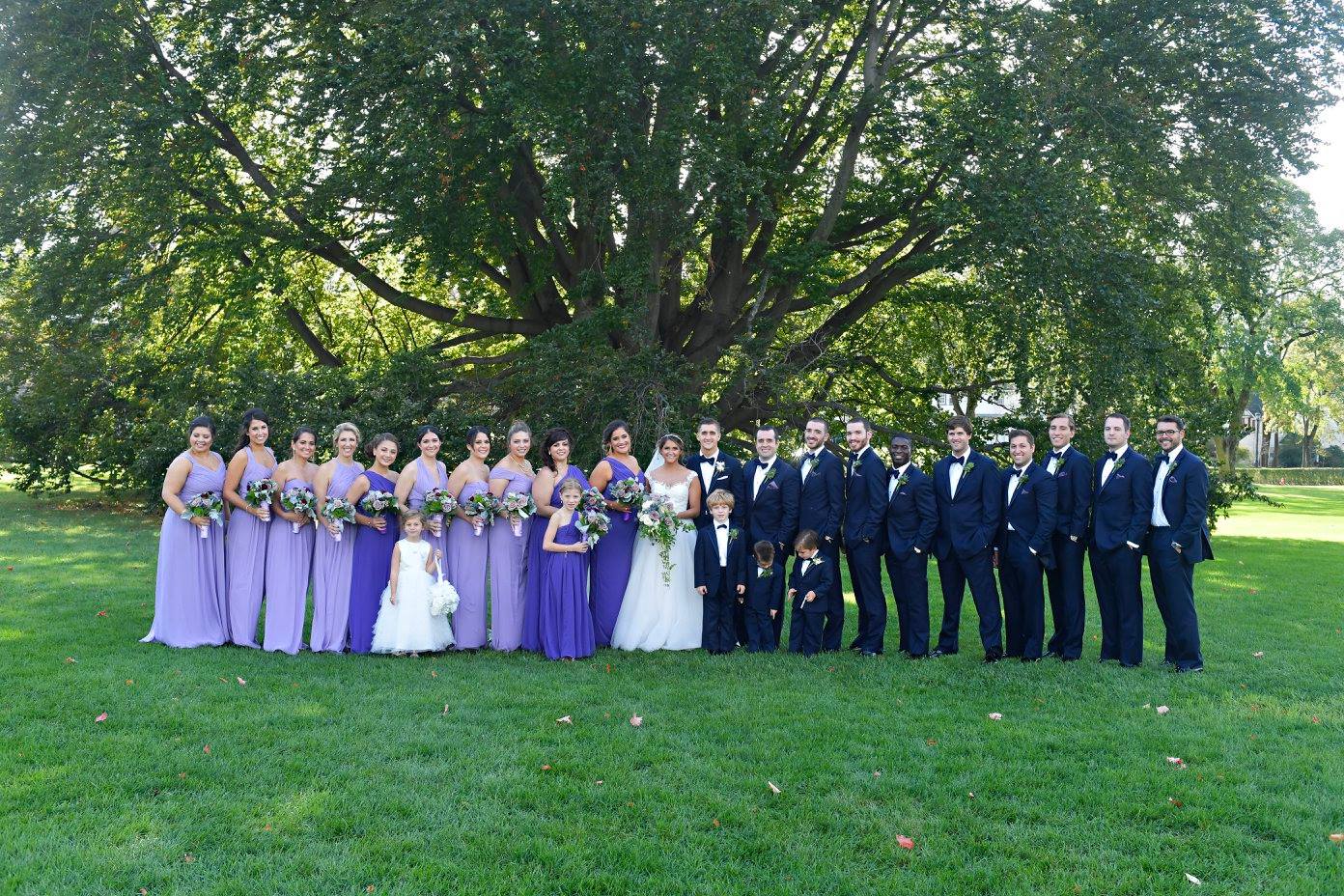 bridesmaids in mismatched purple gowns and groomsmen in black tuxedos