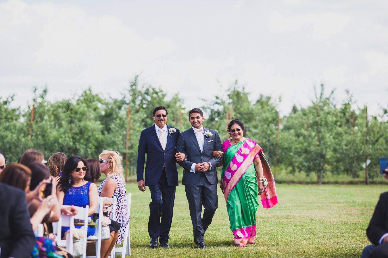 groom walking down the wedding aisle with both parents outside