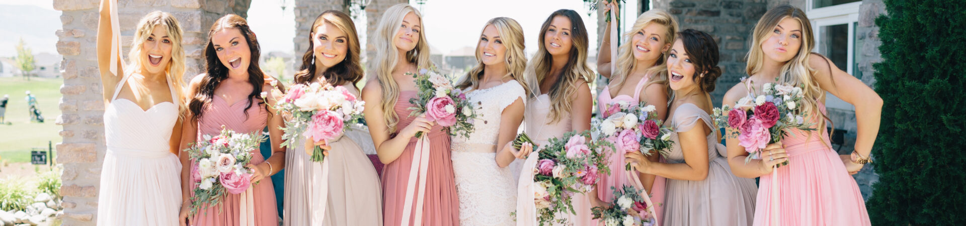 bridesmaids wearing shades of pink lifting bouquets with bride outside