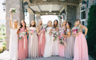 bridesmaids wearing shades of pink lifting bouquets with bride outside