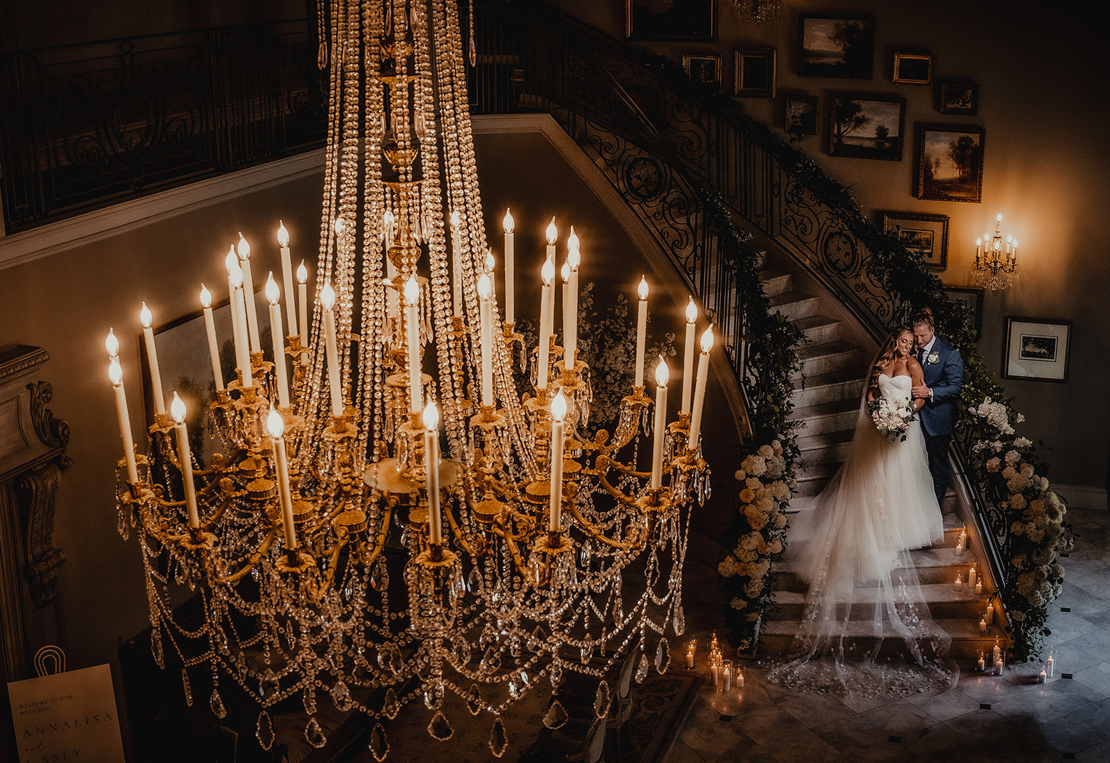 bride and groom standing on stairs with chandelier in front
